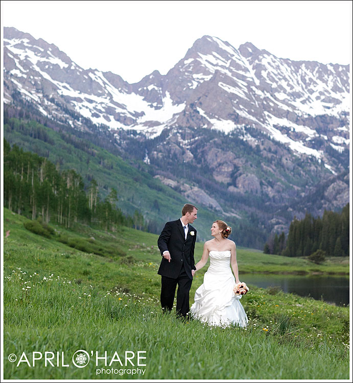 Bride & Groom Walking in a green field in front of mountains