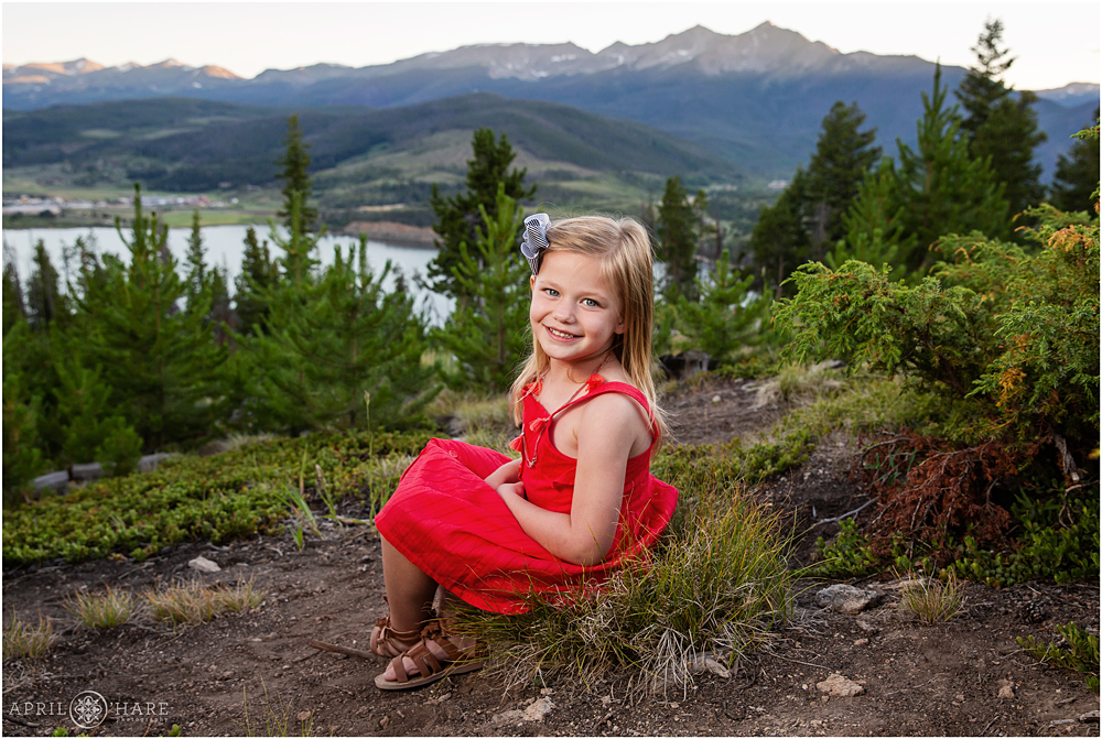 A sweet young girl wearing a red summer sundress poses for a photo with the Ten mile Range of Breckenridge in the backdrop