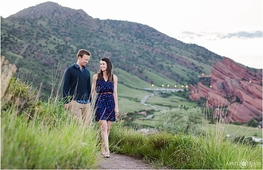 Couple walks along the path with views of Red Rocks behind them at East Mount Falcon for their engagement photography session in Colorado