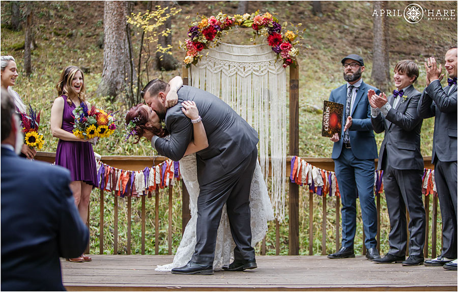 Beautiful Colorado Boho Wedding with macrame backdrop, ribbon garland and fall color floral arch in the woods