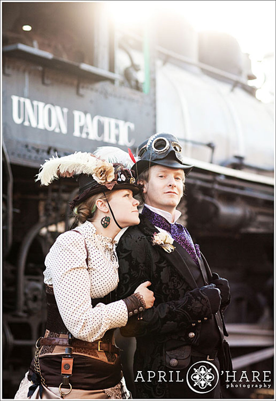 A cute couple dressed in old fashioned Steampunk Victorian clothing pose together in front of an old fashioned Union Pacific railroad train car at the Colorado Railroad Museum in Golden Colorado during their winter engagement session with April O'Hare Photography based in Denver Colorado