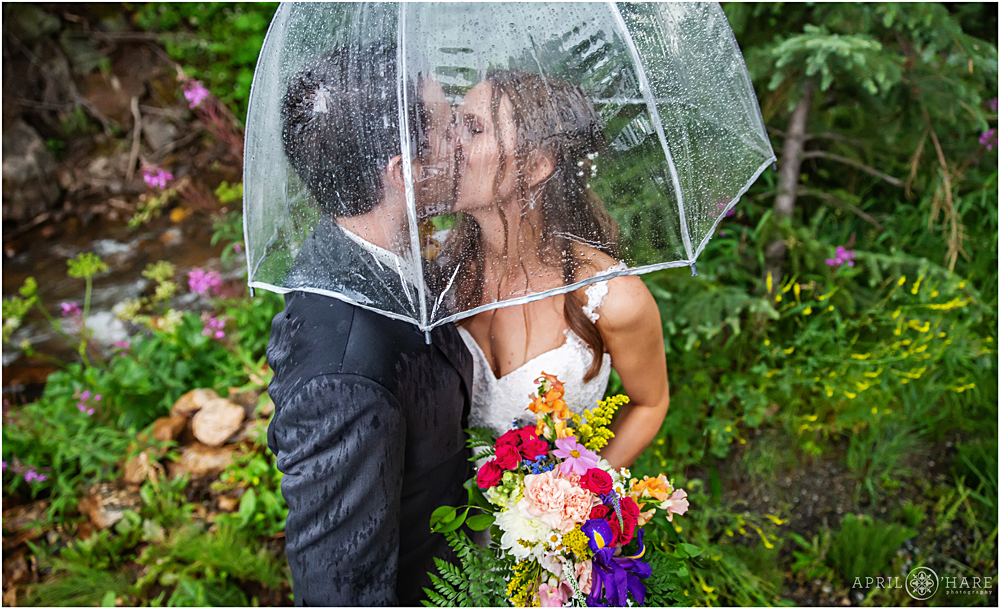 Cute photo of a bride and groom under a clear umbrella on their wedding day at Blackstone Rivers Ranch in CO