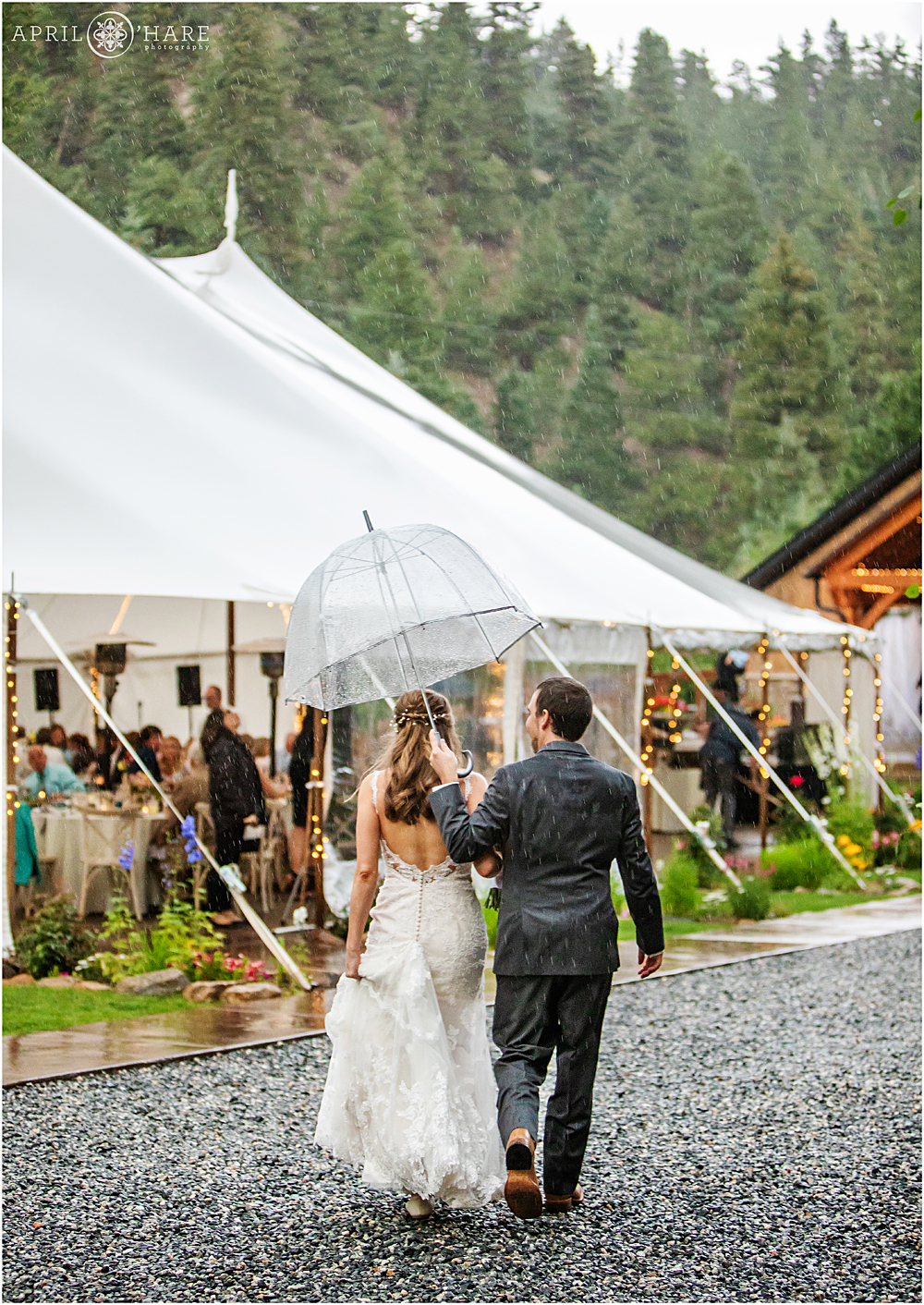 Bride and groom walk back to their reception under a clear umbrella at Blackstone Rivers Ranch in Colorado