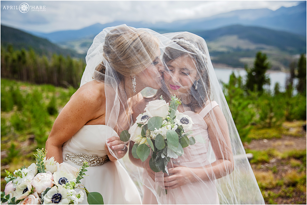 Bride kisses her daughter under her veil with mountain backdrop