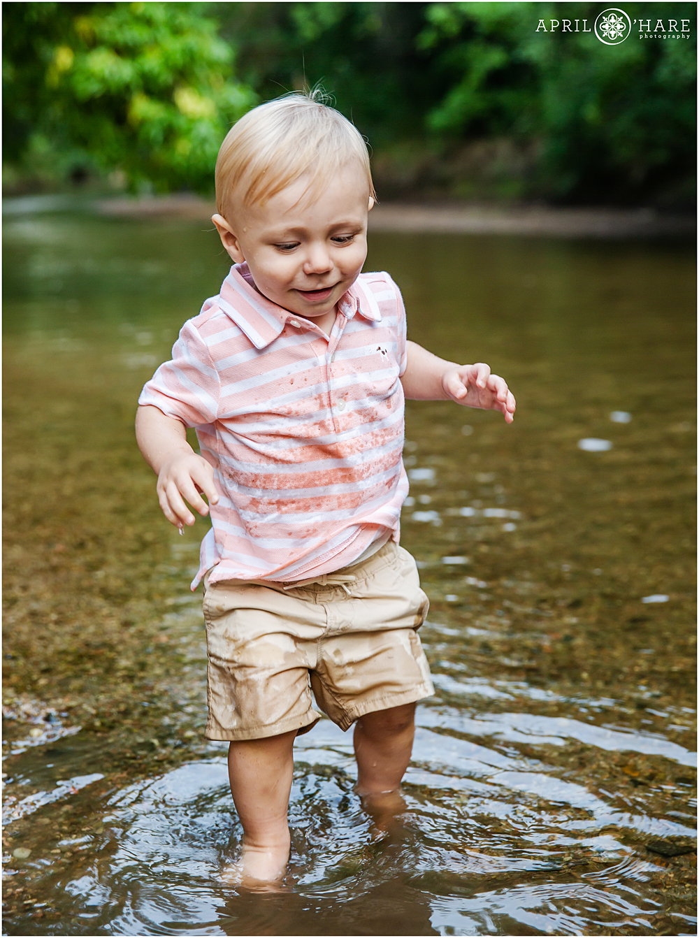 Sweet one year old baby boy plays in the shallow Cherry Creek near Four Mile Historic Park in Denver