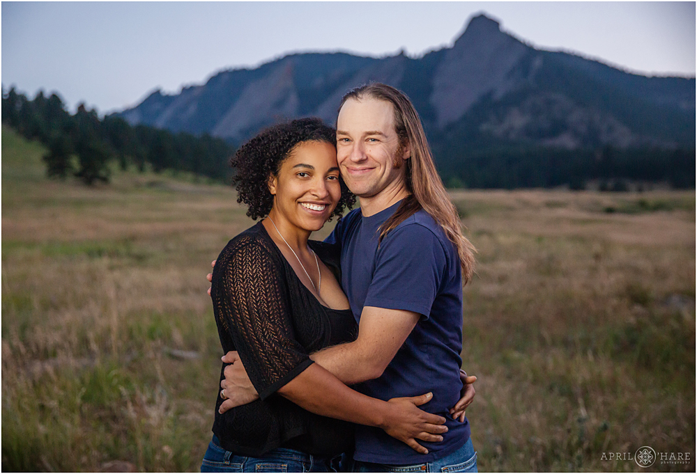 A couple poses for a photo in front of the Flatiron Mountains at Chautauqua at sunset