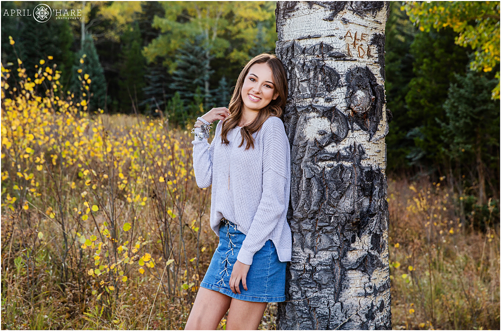 Beautiful high school girl senior photo with aspen tree trunk in Evergreen CO during fall color season