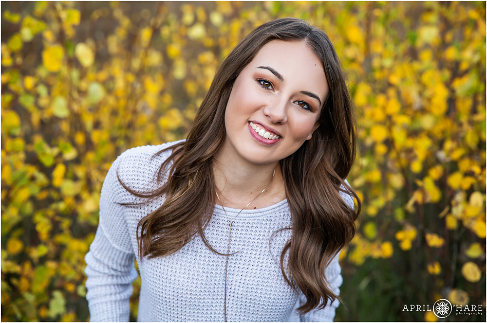 Beautiful headshot of a high school senior in the golden leaves of autumn in Evergreen