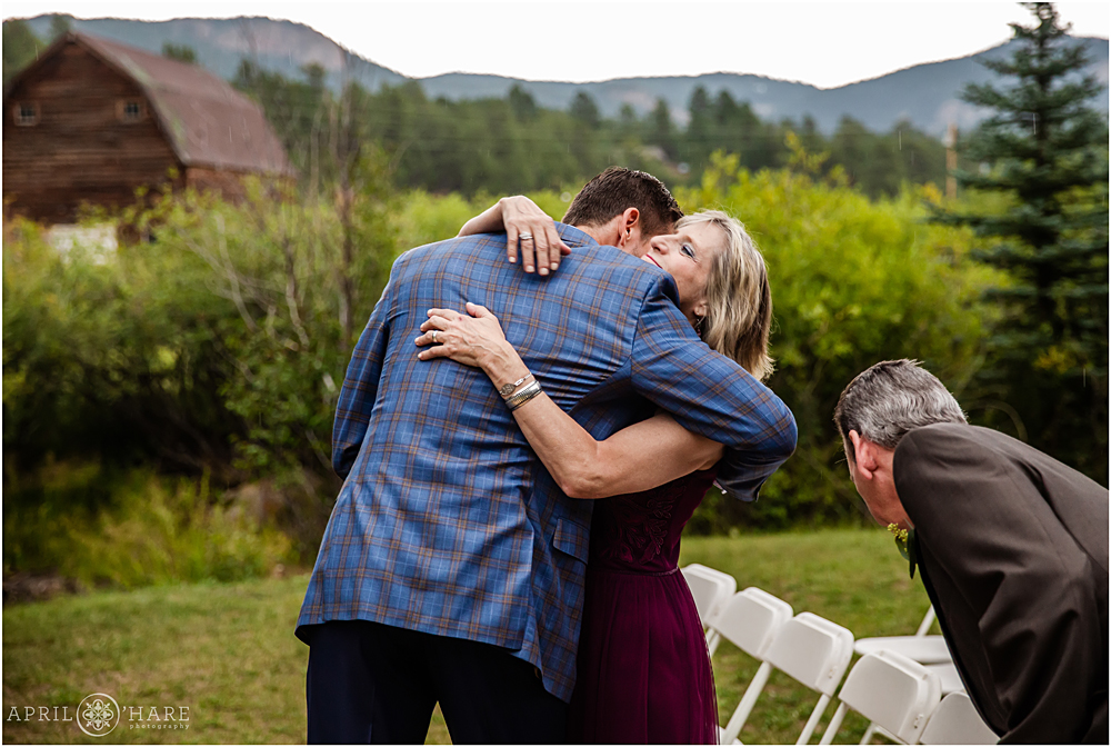 Groom hugs his mom with barn backdrop at outdoor mountain wedding ceremony at Mountain View Ranch in Colorado