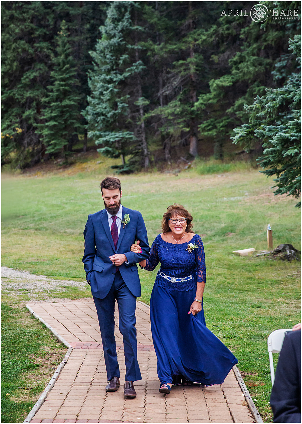 Mother of the bride walks down the aisle with her son at an outdoor Colorado wedding on a stormy summer day