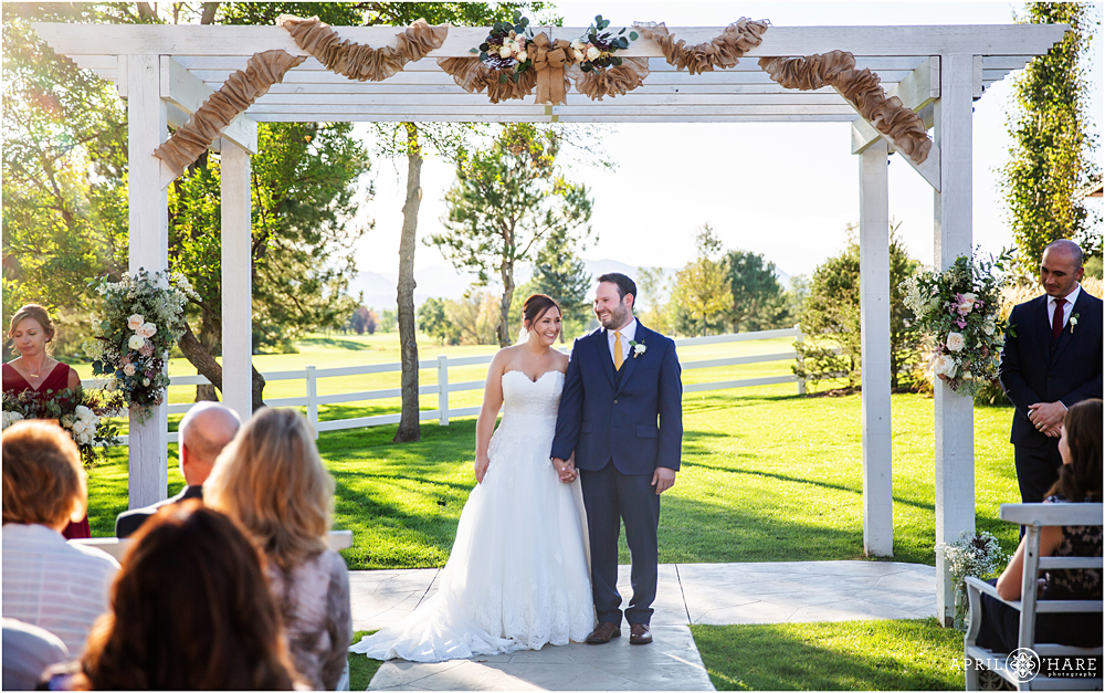 Happy couple stands under the arbor at The Barn at Raccoon Creek