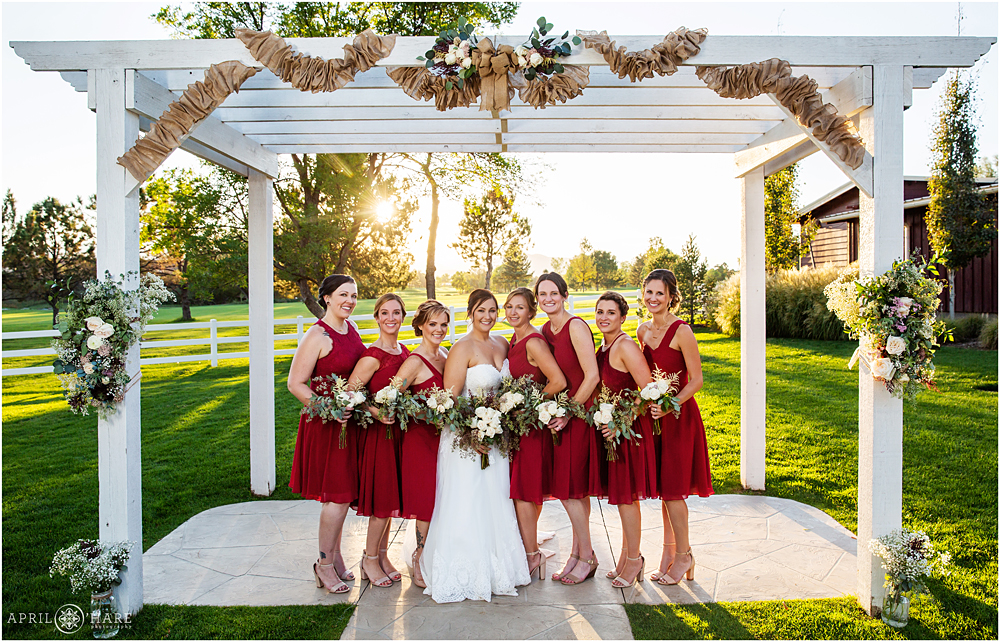 Bridesmaids in Red dresses pose under the wood trellis