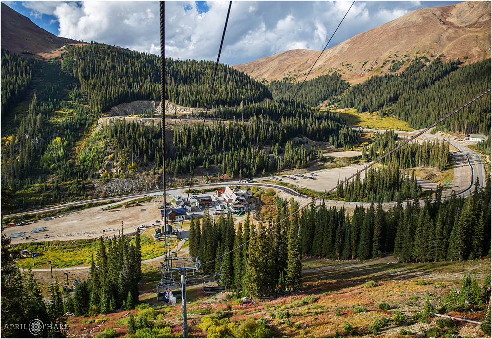A wide view of bride and groom riding the chairlift with A-Basin and Loveland Pass in the backdrop
