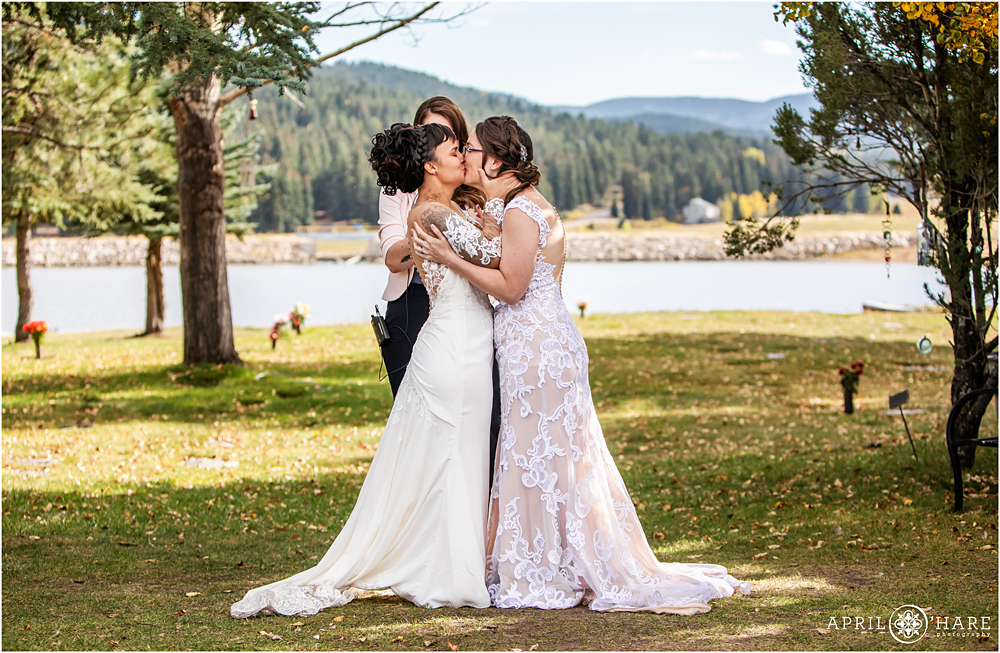 Two brides kiss at their outdoor rustic wedding ceremony at The Barn at Evergreen Memorial Park