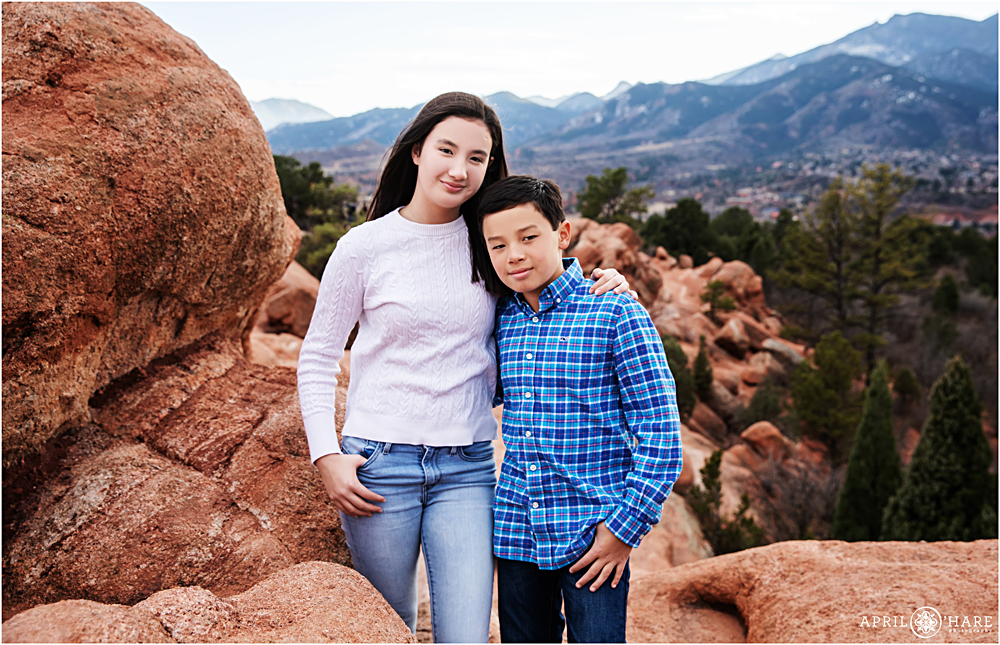 Siblings together on red rocks with blue mountain backdrop at Garden of the Gods in Colorado Springs