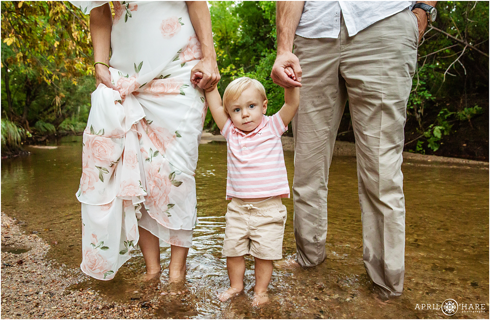 Family holding hands with one year old boy in the Cherry Creek river in Denver 