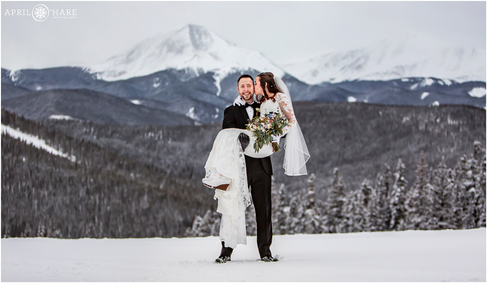 Groom lifts bride in the air as she kisses him on their pretty snowy winter wedding day in Colorado