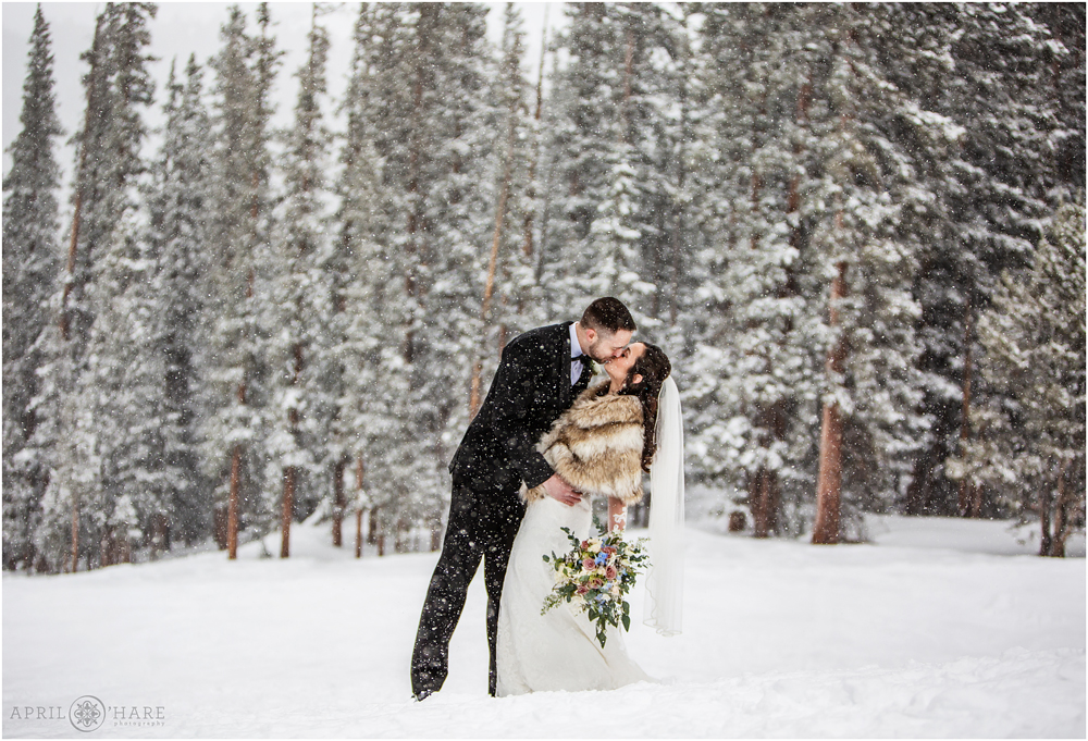 Romantic kiss photo in front of snow covered trees outside of Alpenglow Stube on a winter wedding day at Keystone in Colorado