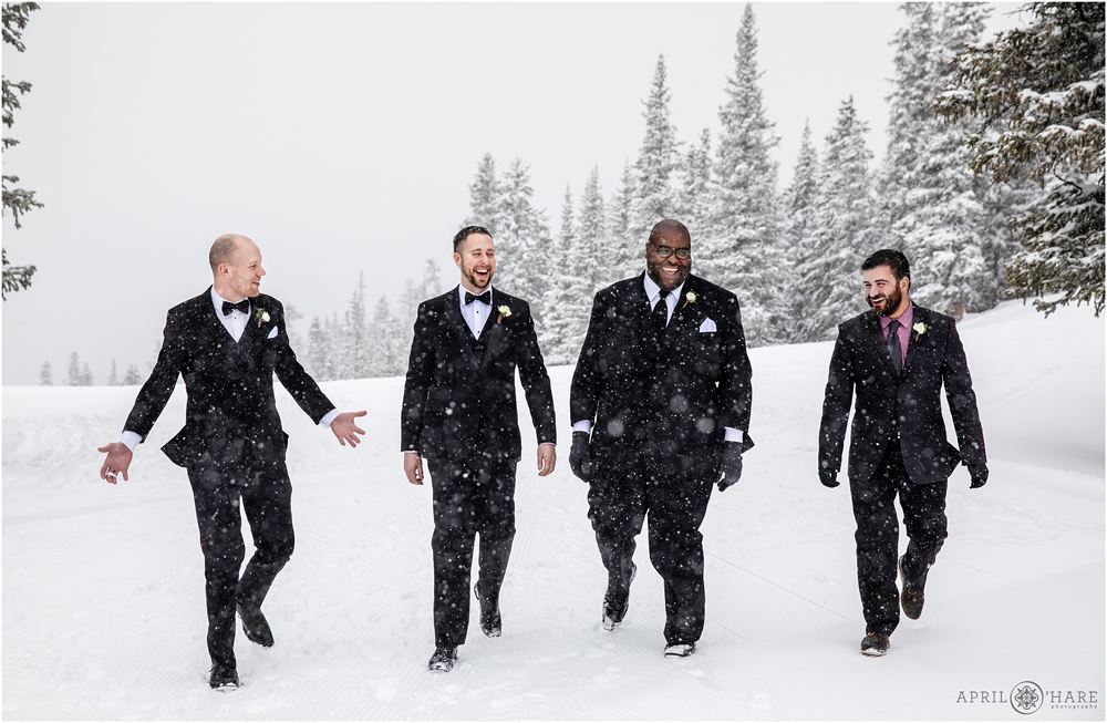 Groom and his friends walk through the snow at his chilly outdoor winter wedding at Keystone Resort in Colorado