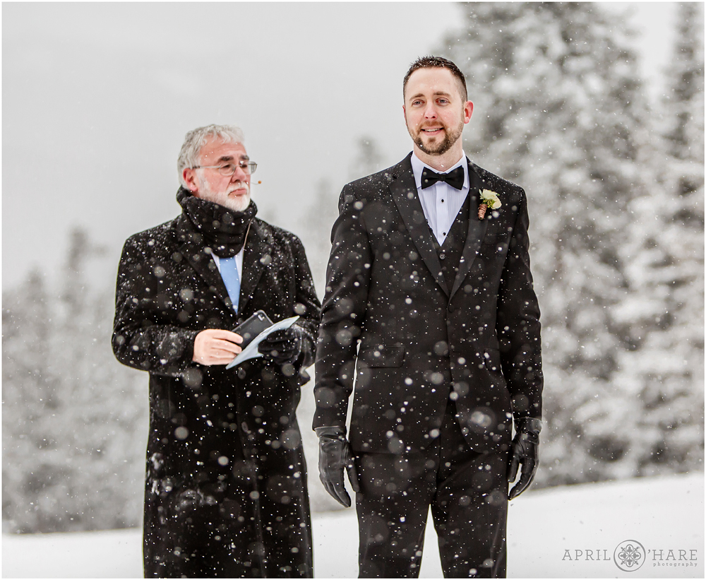 Groom looks at his bride as she walks down the aisle at their outdoor winter destination wedding at Keystone 