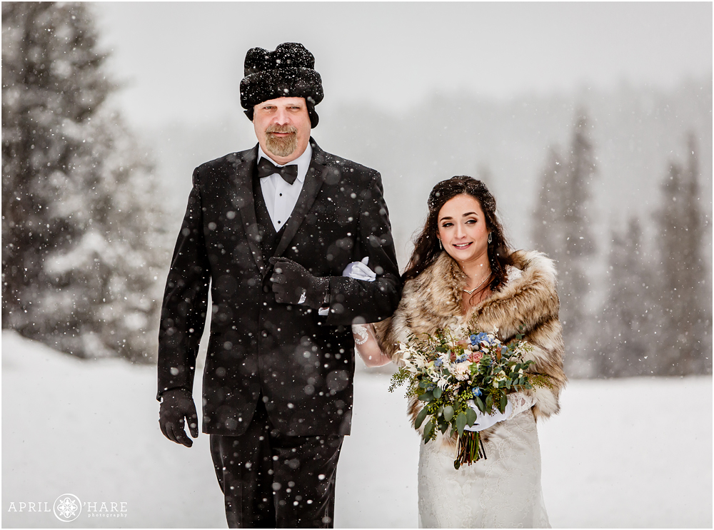Beautiful snowy winter wedding day bride and her dad walk down the aisle at outdoor Colorado wedding at Keystone