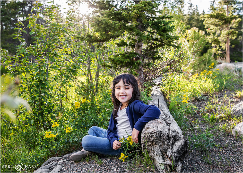 A cute kid poses for a portrait in a woodsy setting with yellow wildflowers at Rocky Mountain National Park in Colorado