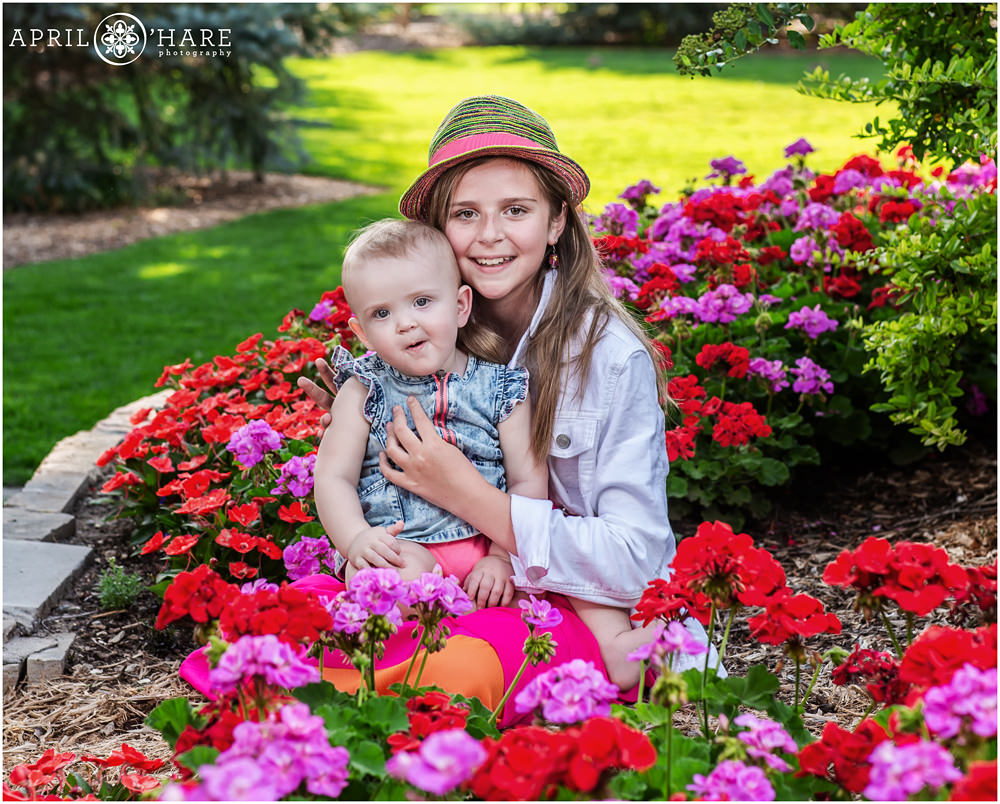 Two sisters pose for a portrait in a pink and red flower garden at Hudson Gardens in Littleton