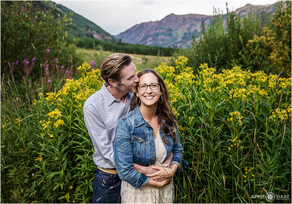 Husband kisses his wife in the huge wildflowers at Maroon Bells in Aspen Colorado