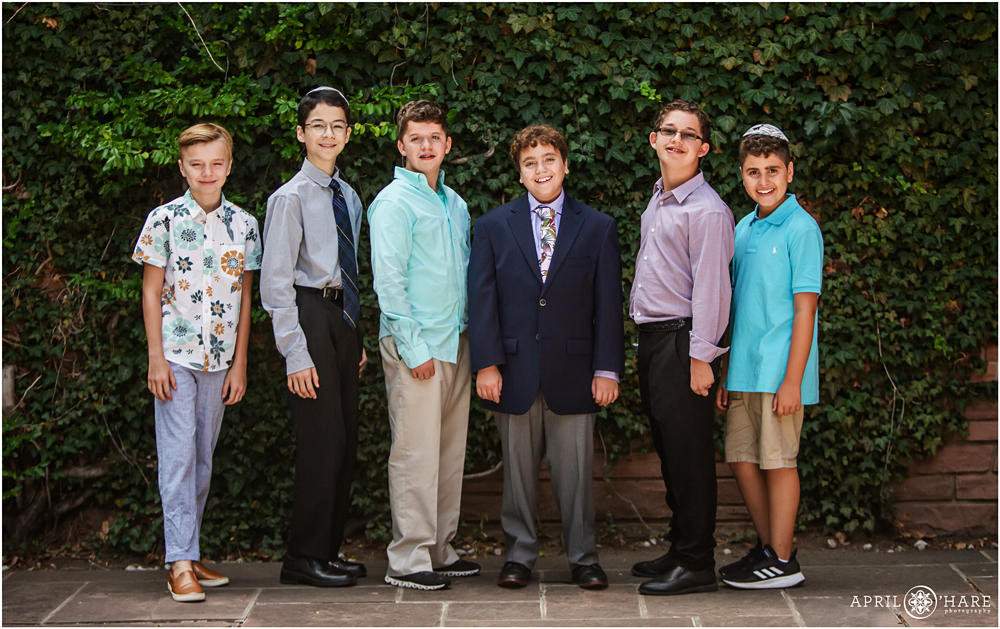 A boy poses for a photo with his friends in front of an ivy wall at his Denver CO bar mitzvah at Temple Emanuel
