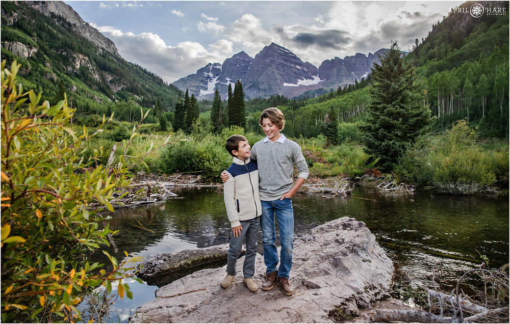 Cute photo of two brothers posing on a rock with Maroon Bells in the backdrop during a family vacation to Aspen Colorado