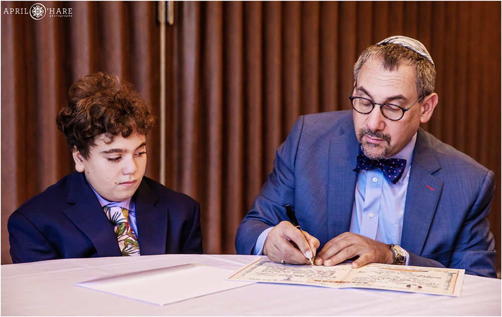 Rabbi and bar mitzvah boy sit down to sign the contract at Temple Emanuel