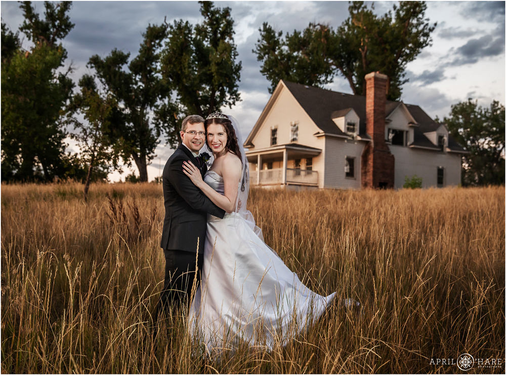 Bride and groom portrait in a field with an old historic white Victorian Farm House at Flyin' B Park in Highlands Ranch