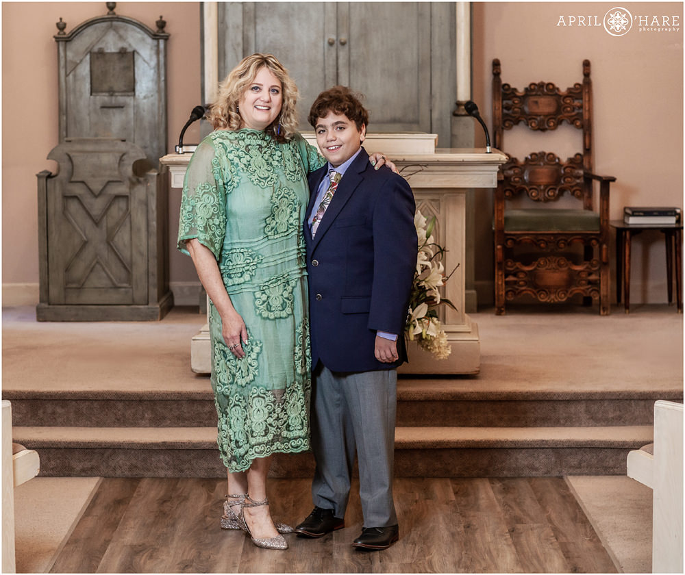 Mom wearing a detailed lace seafoam green dress poses with her son at his bar mitzvah at Temple Emanuel in Denver