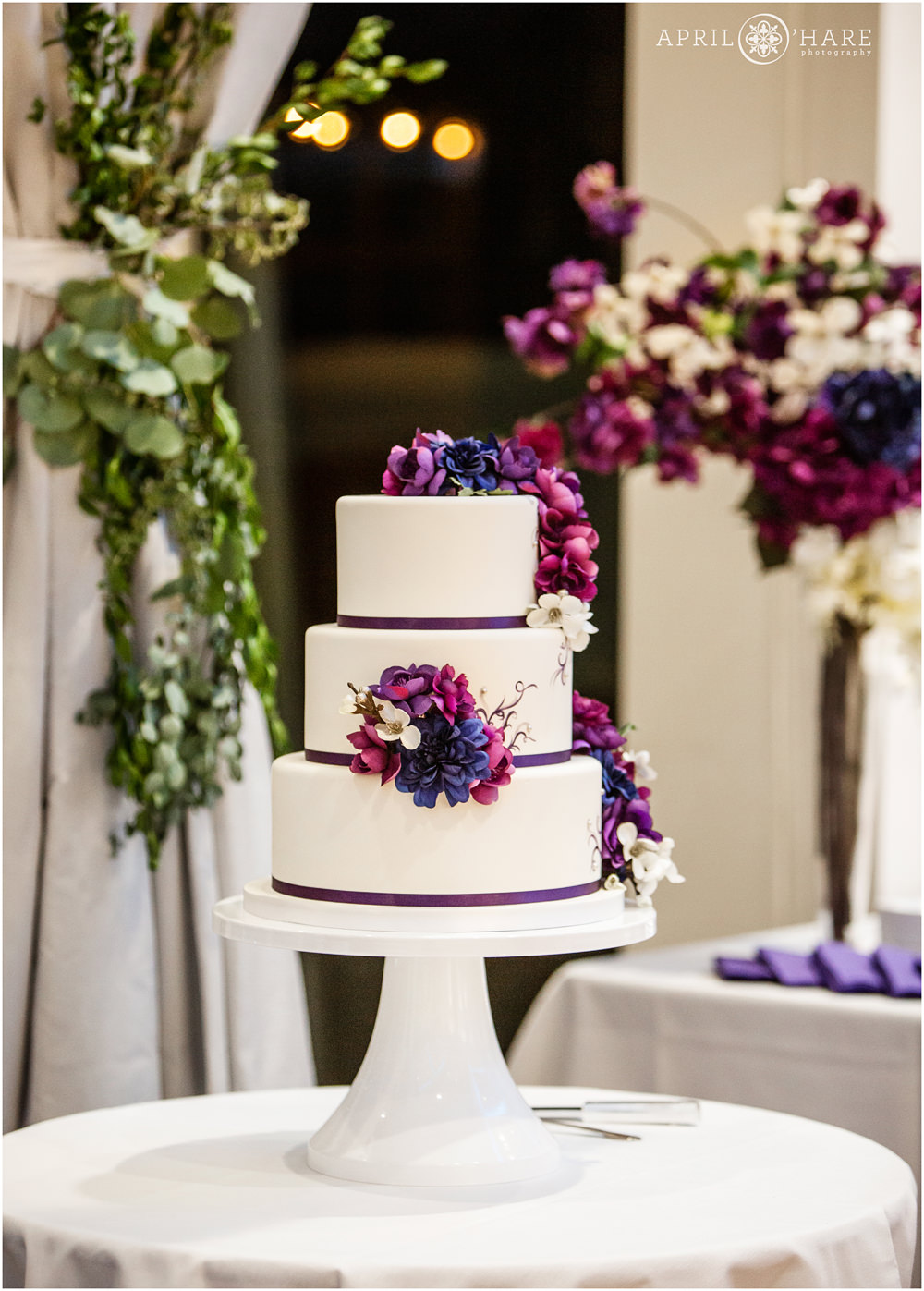 Three tiered white wedding cake with purple florals at Wedgewood Weddings Ashley Ridge Wedding Reception in Highlands Ranch Colorado