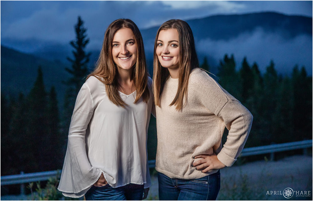 Sisters wearing cream and white pose on the side of the road at a Misty Mountain Family Photography Session in Evergreen
