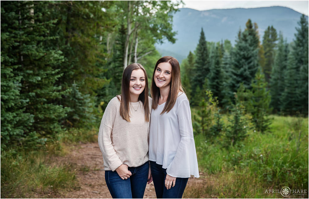 Two sisters pose in an aspen tree forest with mountain backdrop in Evergreen Colorado