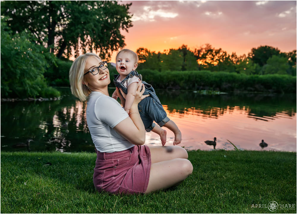 A mother holds her daughter up in the air with pretty sunset sky and swimming duck backdrop