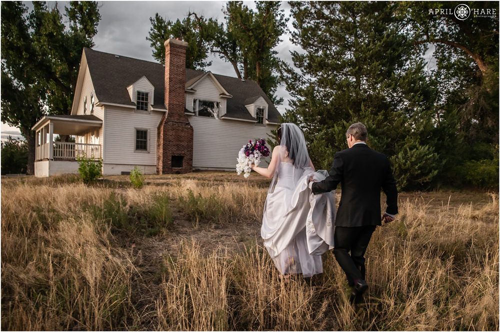 Bride and Groom walk through field with historic house backdrop at Flyin' B Park in Highlands Ranch