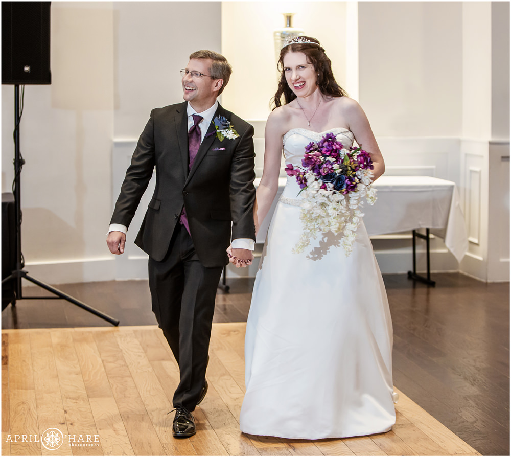 Bride wearing tiara holding purple bouquet walks hand in hand with her groom at Ashley Ridge in Littleton Colorado