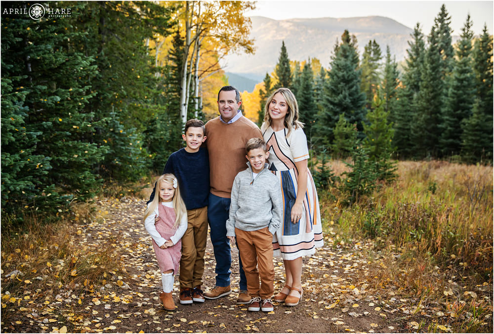 Family of five wearing tan, blue, and pink pose in a fall color mountain environment in Colorado