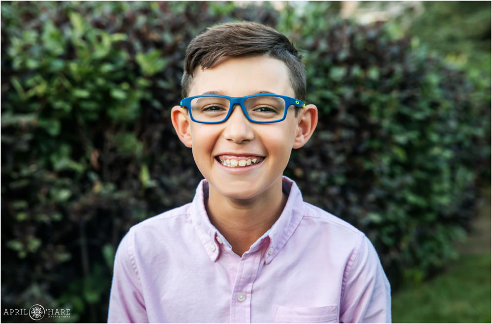 Young boy wearing blue glasses and pink dress shirt poses for an individual picture at his family's at home session in Denver