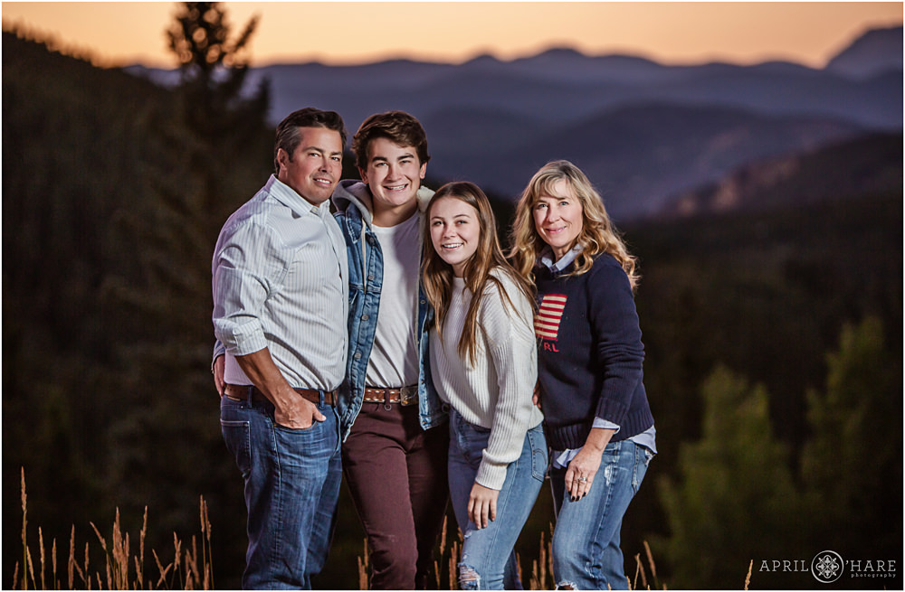 A family of four wearing blue and white pose for photos with a pretty sunset mountain backdrop on Squaw Pass Road in Evergreen