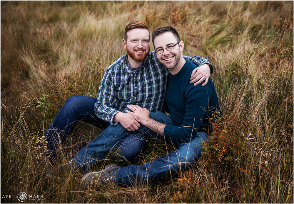 Beautiful fall color gay engagement photo with rich colors and two men wearing shades of blue sitting in a grassy mountain meadow in Colorado