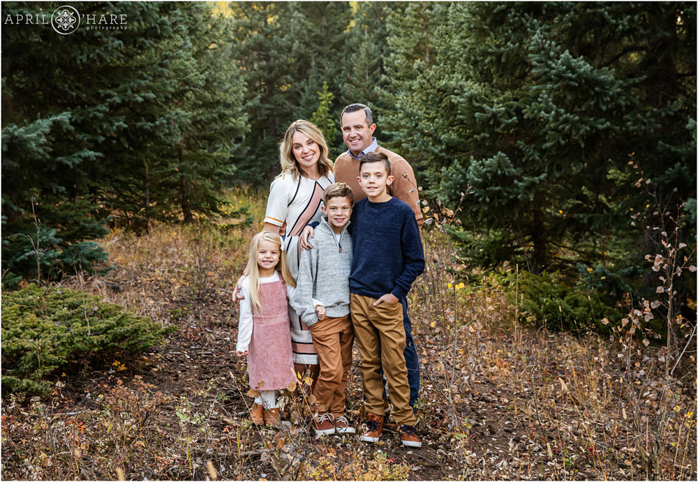 A classic family portrait for a family of 5 standing in an evergreen forest in Colorado