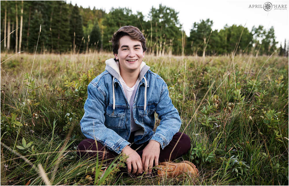 A casual portrait of a high school senior boy sitting cross legged in a Colorado mountain meadow