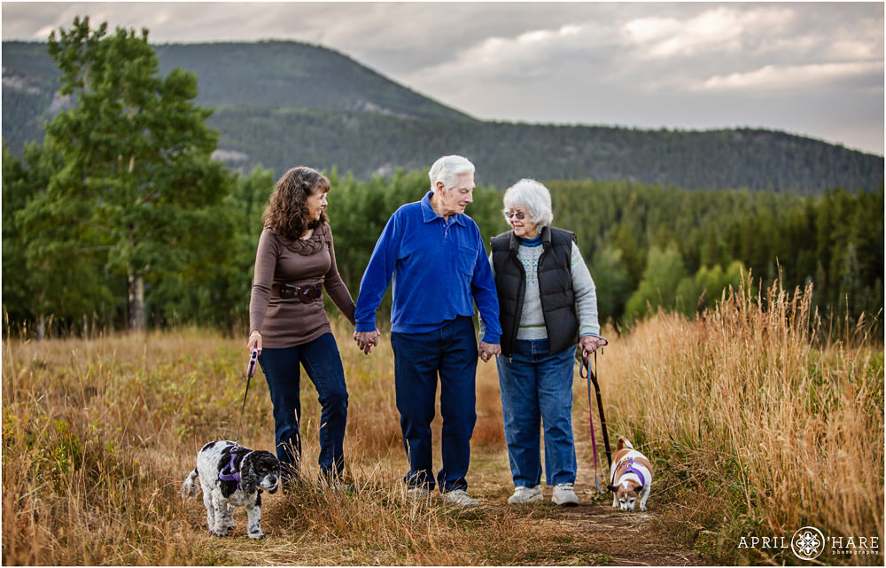 Adult woman walks hand in hand with her parents and their dogs in a Colorado mountain meadow during fall