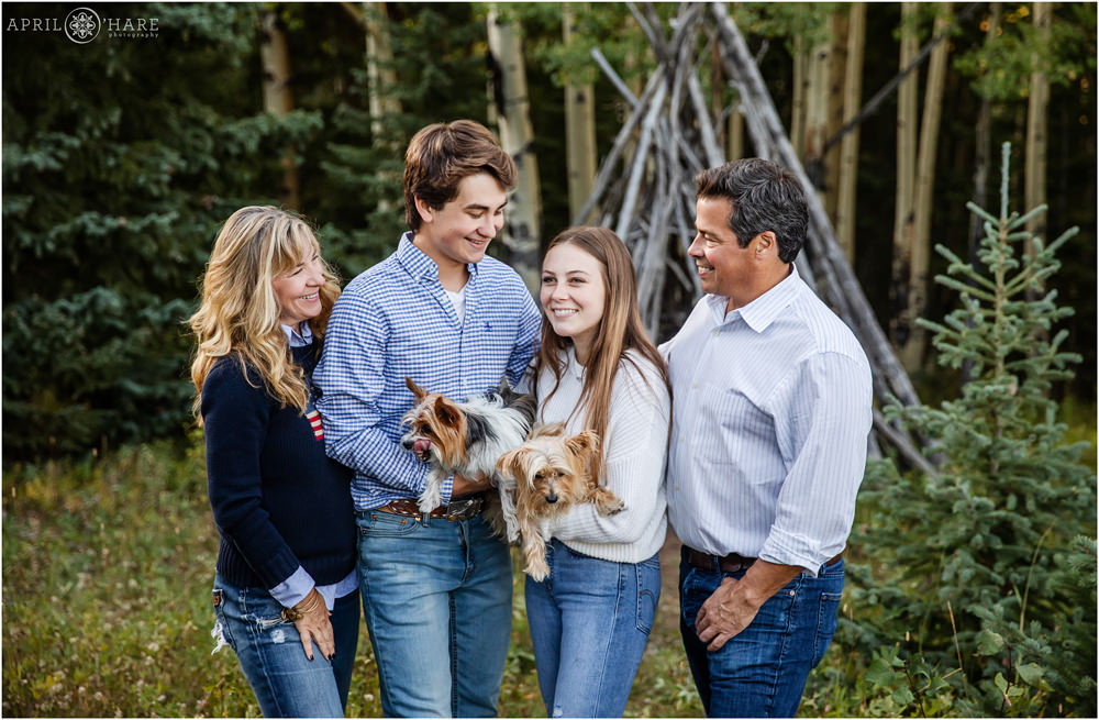 Family of four with two little dogs candid photo in front of wood tipi structure in Evergreen Colorado