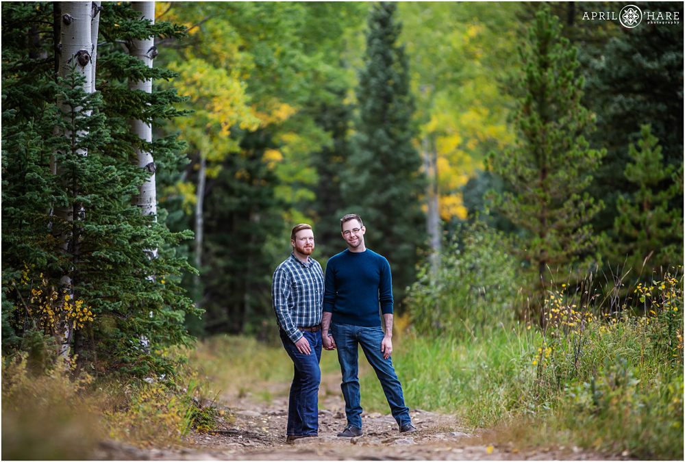 Two handsomemen wearing blue pose on a Colorado mountain forest path during fall color season