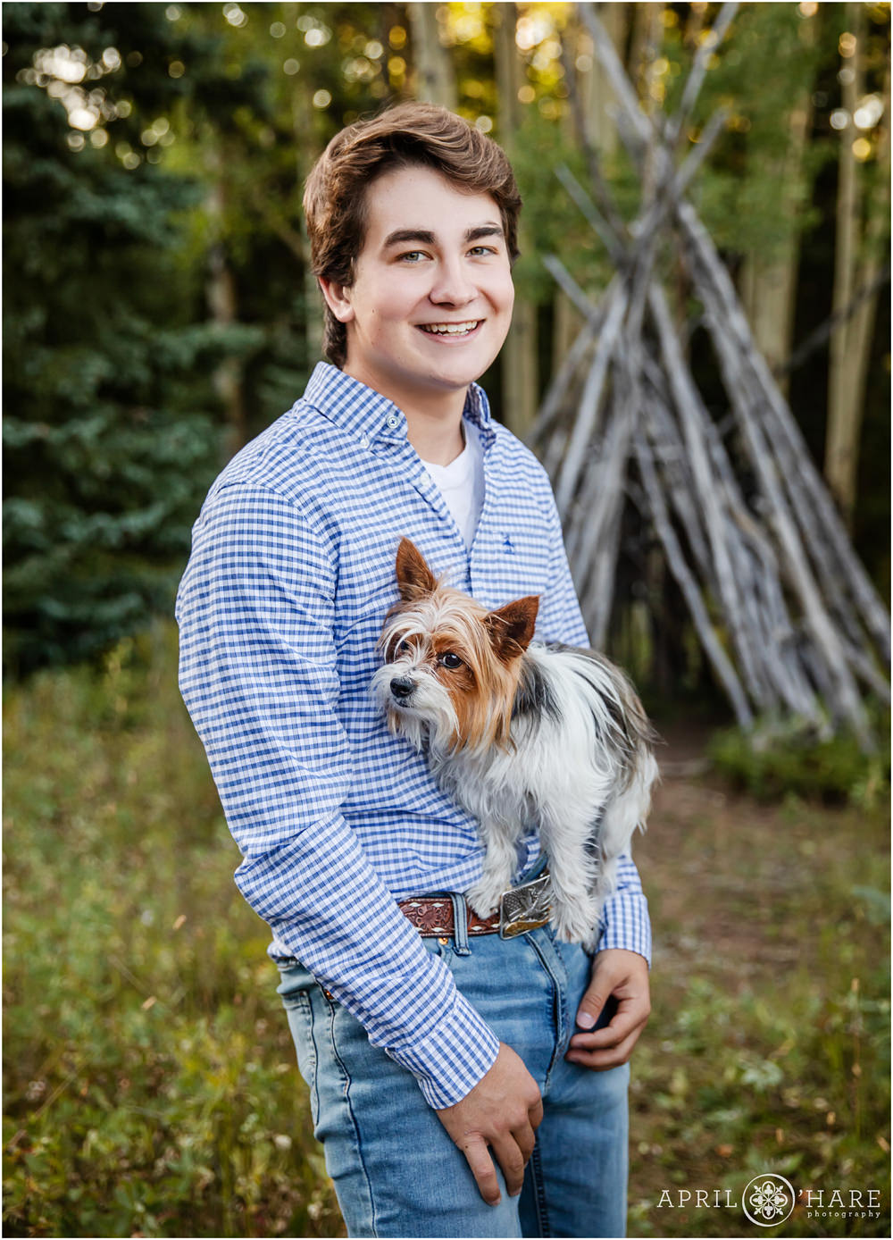 High School Senior Boy smiles as his little dog balances on his belt buckle during his Colorado senior photography session in the mountains