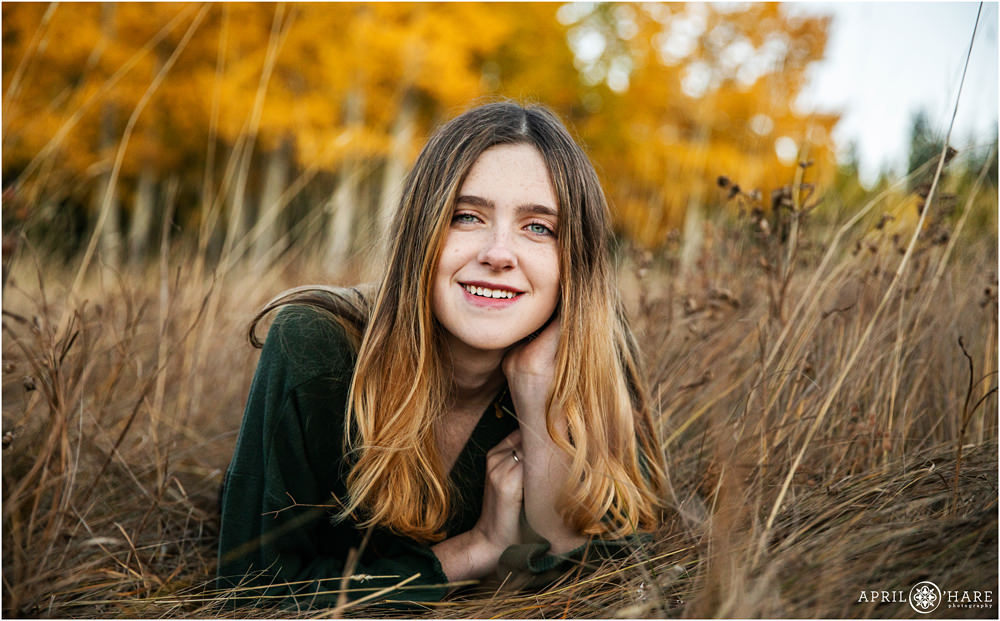 Beautiful fall color senior portrait of a girl wearing a dark green sweater lying in a fall color mountain meadow on Squaw Pass Road in Colorado